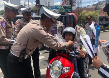 Anggota Satlantas Polres Sukabumi Kota saat memberikan helm gratis kepada seorang anak di sekitar Bundaran Adipura, Kecamatan Cikole, pada Rabu (12/2/2025). Foto: Nuria Ariawan.