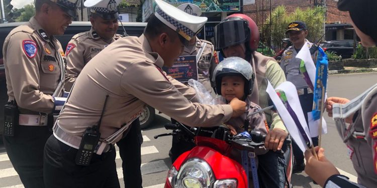 Anggota Satlantas Polres Sukabumi Kota saat memberikan helm gratis kepada seorang anak di sekitar Bundaran Adipura, Kecamatan Cikole, pada Rabu (12/2/2025). Foto: Nuria Ariawan.
